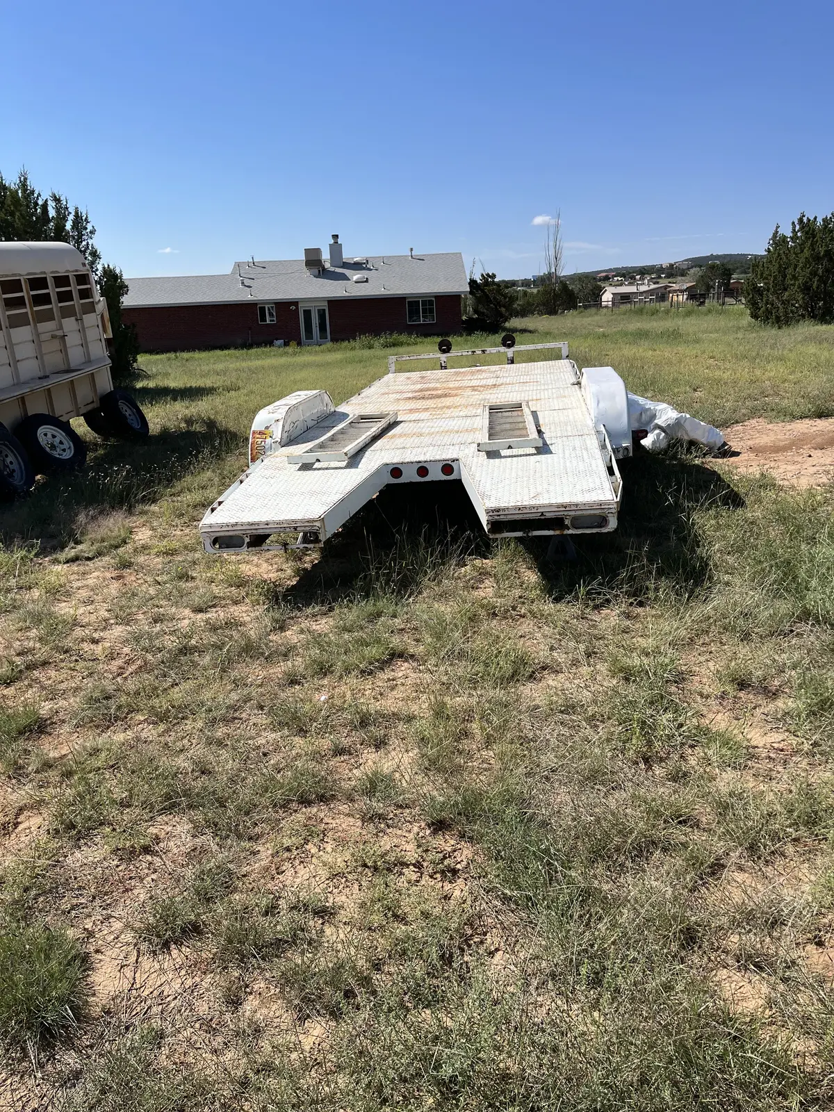 Car-hauler trailer before preparation, with weathered white paint and rust across its diamond-plate deck.