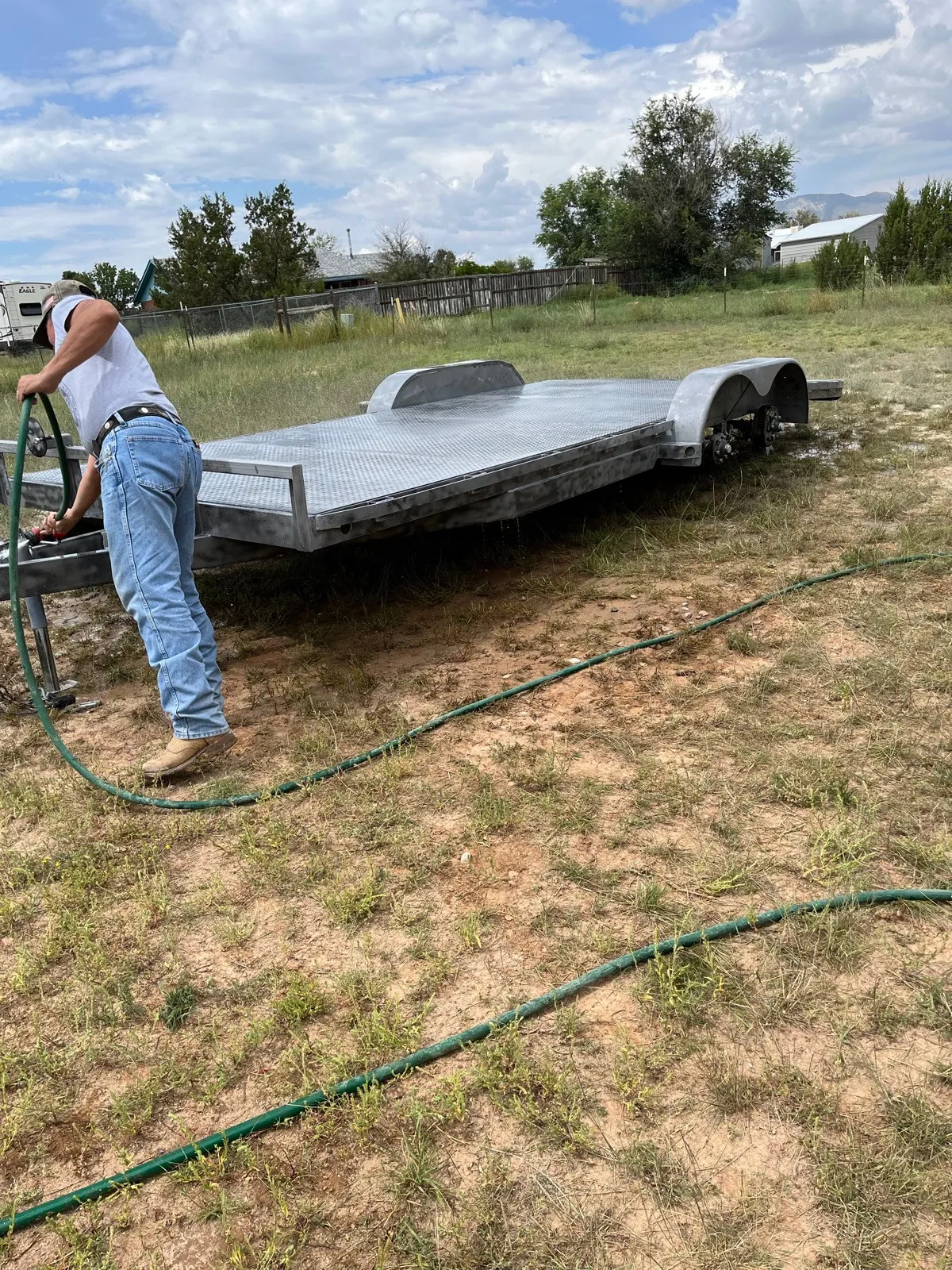 A man rinsing a blasted car-hauler deck with a garden hose.