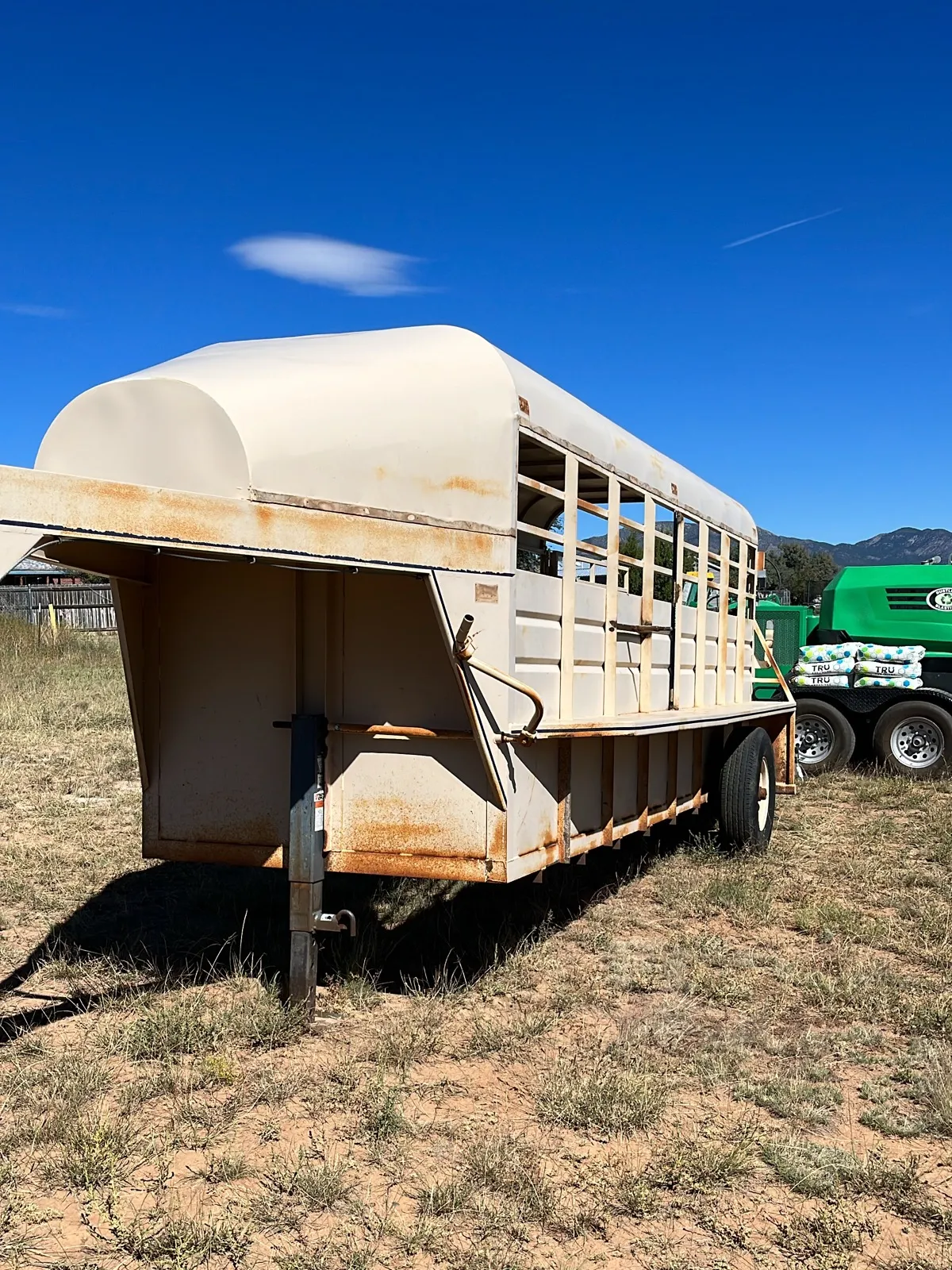 A stock trailer in chalked tan paint with rust starting at the seams.